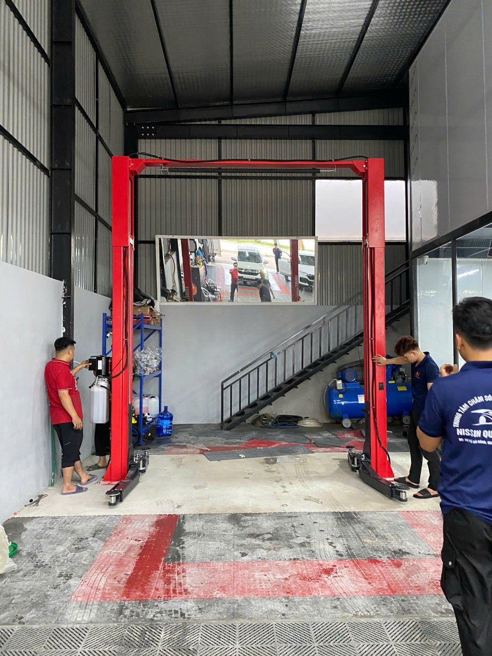 Kỹ thuật viên lắp đặt cầu nâng 2 trụ màu đỏ trong xưởng dịch vụ